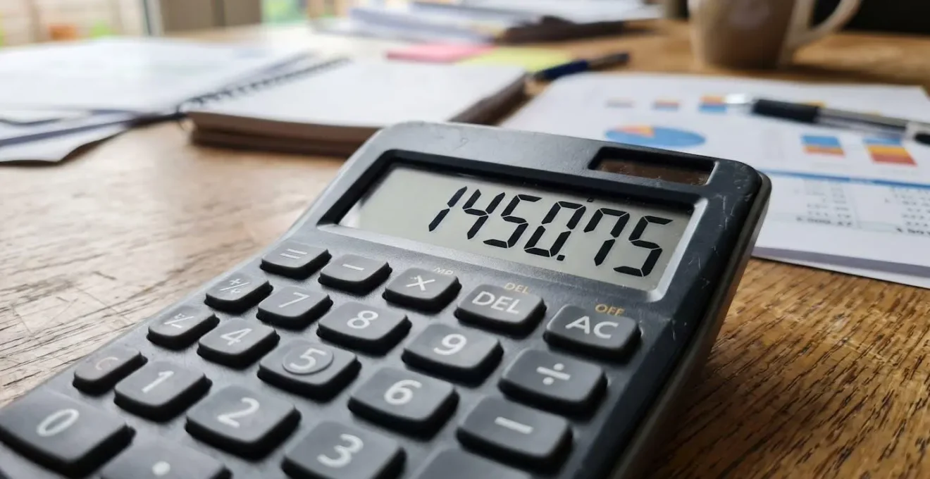 Gros plan d'une calculatrice affichant des chiffres avec en arrière-plan un écran d'ordinateur montrant un graphique de rendement locatif flouté